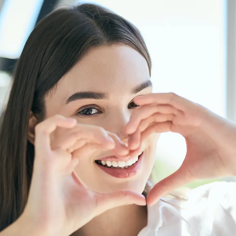 Smiling young woman forming a heart with her hands, showcasing the confidence and happiness gained from a beautiful smile, courtesy of Onyx Dentistry in Vaughan.