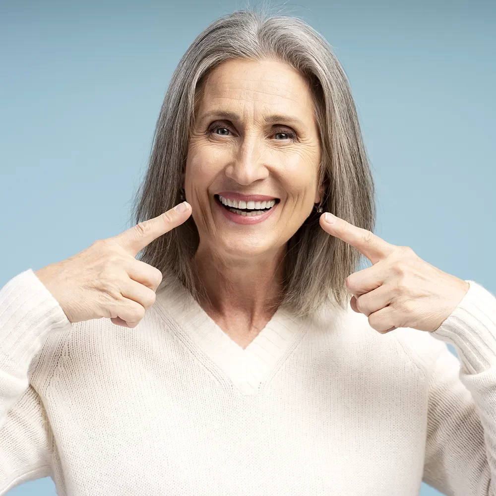 Happy senior woman smiling confidently and pointing to her bright, healthy smile, showcasing the successful dental care and cosmetic treatments at Onyx Dentistry in Vaughan.